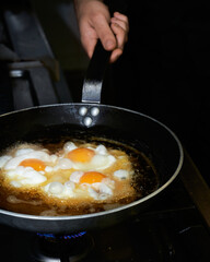 The cook prepares fried eggs in the kitchen. Low key concept of preparing delicious brunch with space for recipe or menu.