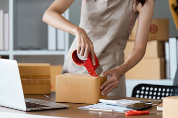 Young business entrepreneur sealing a box with tape. Preparing for shipping, Packing, online selling, e-commerce concept