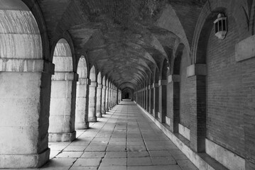 Symmetrical corridor with arches and columns of the royal palace of Aranjuez in black and white.