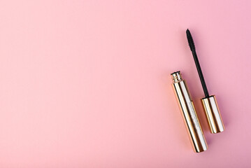 Black mascara in golden tube on pink background.