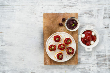 Red tiny cherry peppers stuffed with tuna, served on a plate with tapenade and black olives on a white wooden background, copy space. Top view. Italian antipasti or Spanish tapas concept.