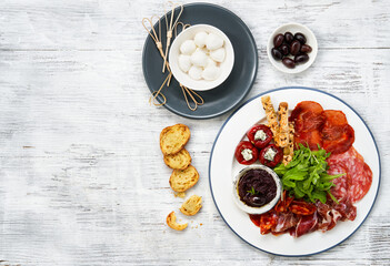 Italian antipasti or Spanish tapas panorama. Gourmet cold meat and Red tiny cherry peppers stuffed with cheese on a plate, top view, white wooden background. Copy space for text.