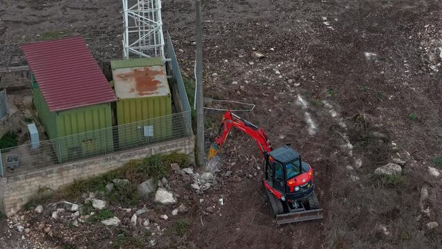 Drone hyper lapse of a mini excavator hammering the foundation of a light pole.
