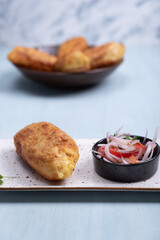 Close-up of golden potato stuffed with tasty stuffing, accompanied by an onion and tomato salad.