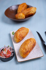 Appetizing Peruvian starter: crispy stuffed potatoes on a plate, accompanied by an onion and tomato salad.
