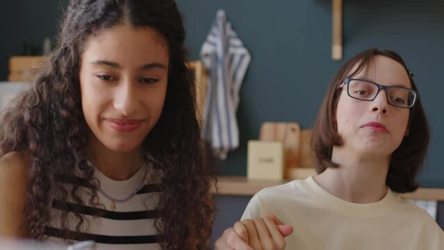 Chest up of two multiracial teenage girls holding hands and singing together at home. Caucasian girl with cerebral palsy having good time with friend indoors