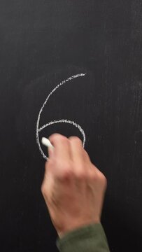 Hand writes the number 6 with white chalk on a black board. Vertical video