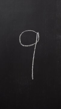 Hand writes the number 9 with white chalk on a black board. Vertical video