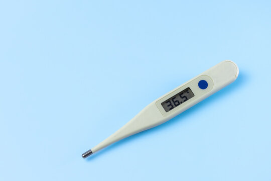 A thermometer with a digital readout of 36.5. The thermometer is white and sits on a blue surface