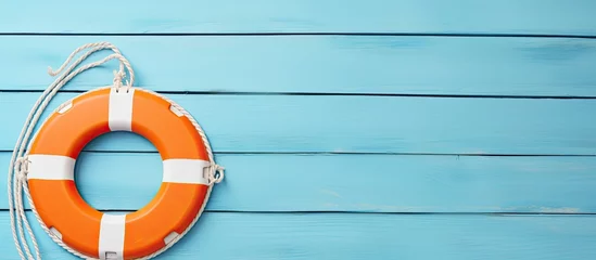 A copy space image of a decorative nautical style on a pearl blue wooden background depicts the concept of water safety with an orange lifebuoy hanging from a white cord