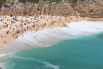 Group of people gathered on a sandy beach surrounded by cliffs and the tranquil waves of the ocean