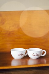 Pair of porcelain mugs arranged on top of a wooden table against Christmas bokeh lights