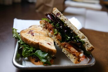 Sandwich on a plate, surrounded by freshly cut lettuce, placed on top of a rustic wooden table