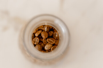 Small glass jar filled with roasted coffee beans on a white table