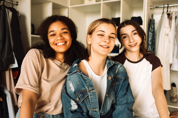 Fototapeta premium Close-up of three cute girls of different races and nationalities in the dressing room at home. Attractive female students are shopping at the store.