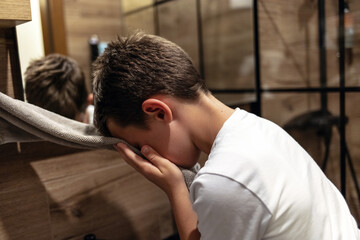 Boy drying his face with a towel in the toilet. Morning boy wiping his face white soft towel after...