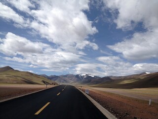 a black road in an open space surrounded by mountains and clouds