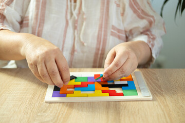 Mature female hands manipulate wooden geometric shapes intellectual puzzle, potential mental...