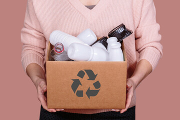 Woman holds cardboard box filled with plastic waste, promoting eco-consciousness and responsible...