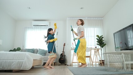 Caucasian mom and asian child doing housework together and dancing to music. Attractive mother and...