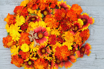 Fototapeta premium orange-red colorful flowers and wooden christian cross on table. Symbol of the death and resurrection of Jesus Christ, Faith of God, Hope, Love. Religious church holiday. top view. close up