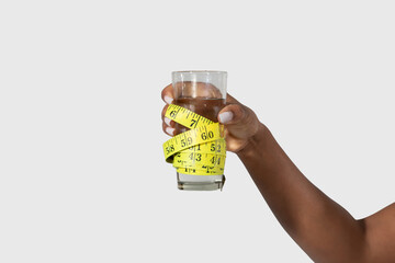 Cropped of black woman is shown holding a measuring tape up to a glass of water, possibly measuring the height or volume of the liquid, white background
