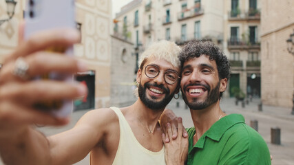 Gay couple stands hugging and makes video call from mobile phone, waving in greeting