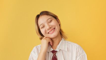 Young woman dressed in shirt and tie laughing while looking at camera isolated on yellow background...