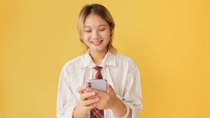 Smiling young woman wearing shirt and tie using mobile phone isolated on yellow background in studio