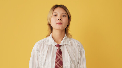 Young woman dressed in shirt and tie listens carefully and agrees isolated on yellow background in...