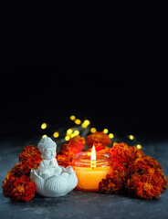 Buddha figurine with orange flowers and burning candle on dark background. esoteric spiritual...