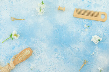 Hair dresser composition with hairbrush, tassel and white flowers on blue. Flat lay, top view