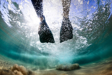 Legs of a swimmer wearing flippers in shallow clear ocean water