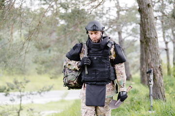 Young soldier in uniforms and tactical vest works in the forest and prepares for action at a...