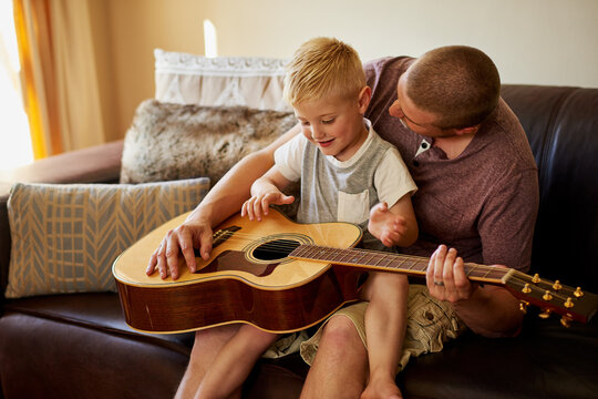 Father, child and learning guitar in home or musical instrument for teaching, bonding or song. Man, son and couch or notes development in family house for weekend lesson with playing, musician or fun