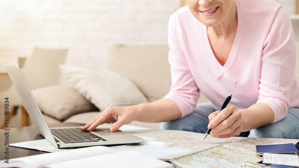 Poster cropped of senior woman is seated on couch, engaged in work on a laptop with focused concentration. 