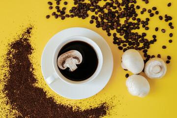 A white coffee cup and saucer stand on a yellow background. A slice of champignon mushroom floats in a cup, and coffee beans and ground coffee are scattered nearby and three champignons lie. mushroom 