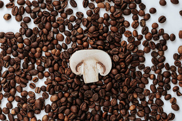 coffee beans are scattered on a light background, and in the center lies a slice of champignon mushroom. shot from above