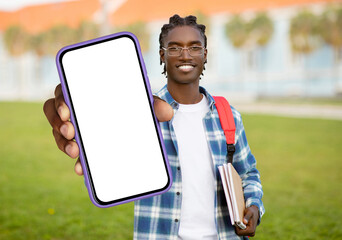 A cheerful young black man with braided hair carrying a red backpack, holds out a smartphone with a...