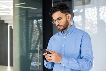 Focused man in blue shirt using smartphone in modern office setting