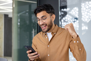 Excited young man celebrating success while looking at smartphone screen