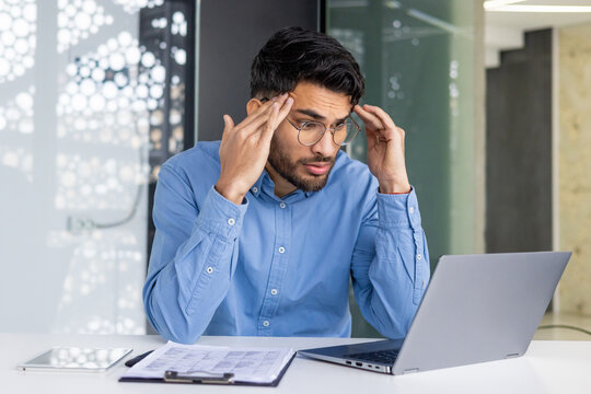 Stressed businessman working on a laptop and holding head in hands in modern office
