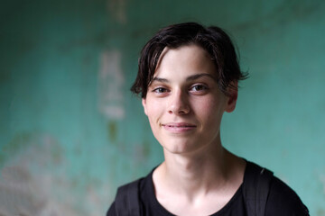 Portrait of a young smiling teenage guy in a black T-shirt against the background of a green old wall on a cloudy rainy day
