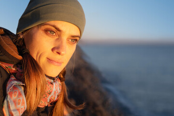 A young thoughtful woman relaxes in the evening on a pebble beach by the sea and looks into the distance at sunset in spring
