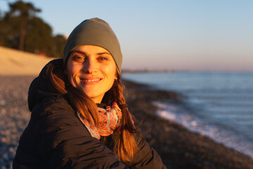 Young pensive woman relaxing in the evening on a pebble beach by the sea at sunset in spring