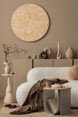 Warm and cozy living room interior with round wall panel, stylish sofa, brown plaid, beige coffee table, vase with dried flowers, books, modern sculpture and personal accessories. Home decor. Template