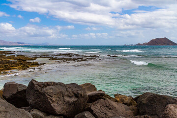 The rocky, volcanic coastline of the Atlantic Ocean near the port of Corralejo. Labos island in the background. Fuerteventura, Canary Islands, Spain