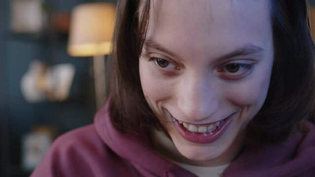 Tilt shot of excited Caucasian teenage girl with cerebral palsy playing video game with controller at home at night