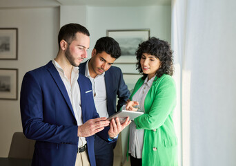 Three people in suits are looking at a tablet