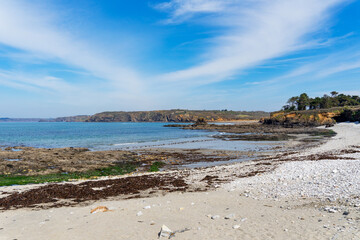 Sur la presqu'île de Crozon, une plage de galets s'étend sous un ciel bleu éclatant.